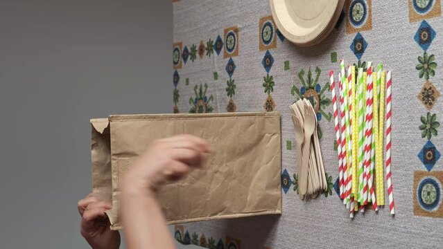 hand picks up biodegradable one-use cutlery from the table to put them in an ecological paper bag
