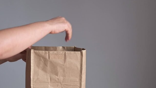 hands introduce disposable and biodegradable one-use cutlery into an ecological paper bag
