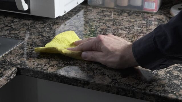 person's hand cleaning stain on countertop with a cloth cloth.
