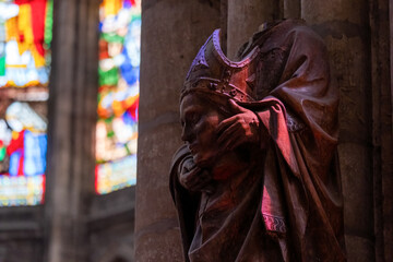 Statue of St. Denis of France holding his own head. Sculpture is bathed in colored light from the stained glass windows of St. Denis Basilica