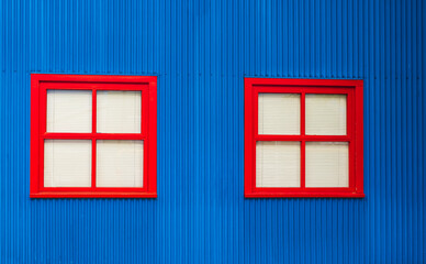 Two windows with red wood frames in a blue color wall. Exterior of a house with windows. Beautiful colorful house facade