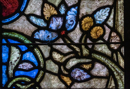 Stained glass window in a cathedral depicting a medieval floral motif. Blues, reds, greens, golds. Detailed painted glass 