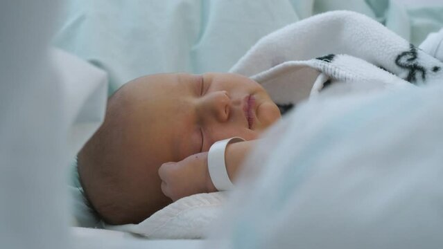 Close-up of calm newborn baby's face sleeping in wrapped in blanket in hospital bed. Real time. Static view
