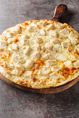 Pizza with creamy homemade alfredo sauce topped with chicken, mozzarella and parmesan cheese closeup on the wooden board on the table. Vertical