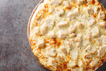 Hot cheese Alfredo pizza with chicken close-up on a wooden board on the table. Horizontal top view from above