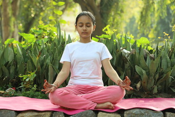 Young Indian female child practicing  yoga in the park in day time. Girl is doing yoga in clean and green environment and fresh air.