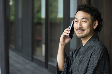 Close-up of a bearded middle-aged handsome Japanese man in a yukata making a phone call or contacting someone on his phone.