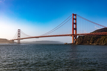 Fototapeta na wymiar The Golden Gate Bridge in San Francisco over the bay of the Californian city under a blue sky and ocean. Famous bridge in the state of California and seen from a viewpoint. Concept USA.