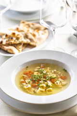 Chicken stock or soup with vegetables and small Italian pasta served on a table