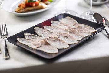 Thinly sliced veal with a tuna salsa served on a black rectangular plate