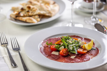 Typical Italian appetizer, carpaccio from veal or beef thinly sliced and served on a plate with salad