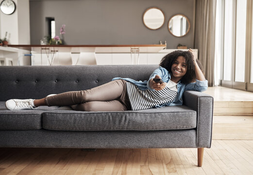 Sofa, African Woman Watching Tv And With Remote On The Couch In Living Room Of Her Home. Entertainment Or Relax, Happiness And Comfortable Black Female Person Streaming Series Or A Movie In Free Time