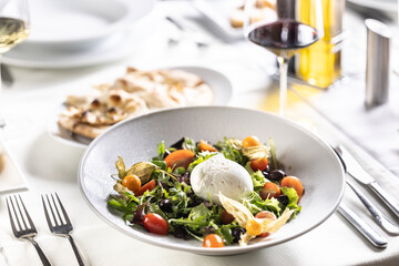 Buffalo mozzerala ball as a centerpiece of a salad with rocket, leaves, cherry tomatoes, physalis and olive oil