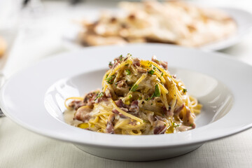 Spaghetti carbonara made with fried bacon cubes, yellow sauce from eggs and sprinkled with greens
