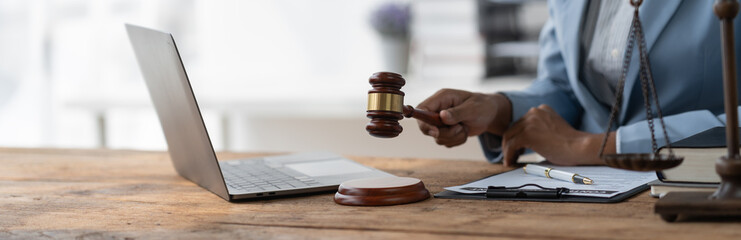 American female lawyer or judge African woman holding a hammer of justice, concluding business contract documents, tax, accounting, justice scales and consulting services legal concept.