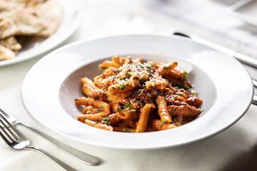 Pene alla arrabiata, Italian red sauce pasta served on a table in a plate with fresh grating of parmesan