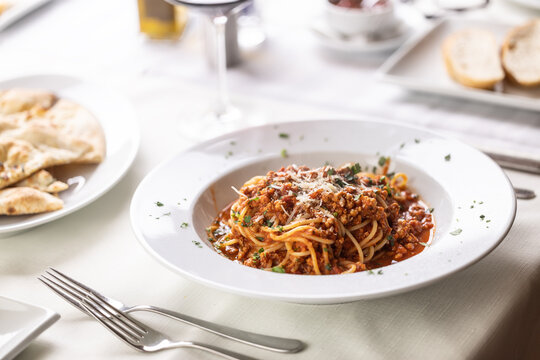 Restaurant serving of spaghetti bolognese with grated cheese on top on a white table