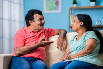 Obraz premium happy Indian senior couple discussing by talking each other while sitting on sofa at home - concept of communication, long relationship bonding and understanding.