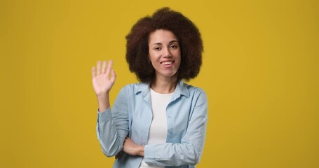 Young smiling african american woman shaking waving hand saying goodbye standing over orange studio background