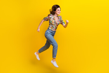 Fototapeta na wymiar Full length photo of running girl wear spring outfit flowers print blouse denim jeans stylish sneakers isolated on yellow color background