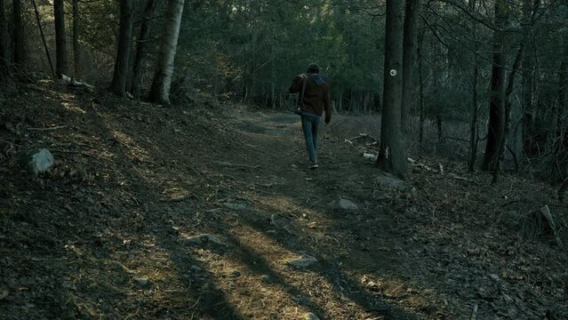 Young photographer walks down wooded path (wide)