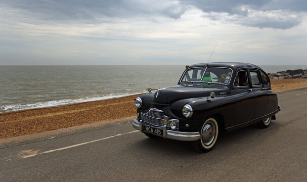 Vintage Black 1951 Standard Vanguard Motor Car being driven on seafront promenade beach and sea in the background.