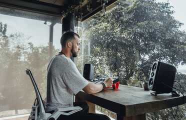 young handsome man with a beard and dark hair sits at a table and creates music, listens to headphones, writes songs, musician portrait, concept, laptop, monitor speakers, pianist, recording studio