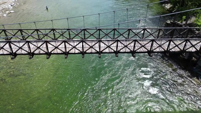 Drone flight over a wooden Tibetan suspended bridge that joins the river banks - view from the drone in Alagna Val Sesia Piedmont Alps mountains - travel concept journey in adventure natural trip 