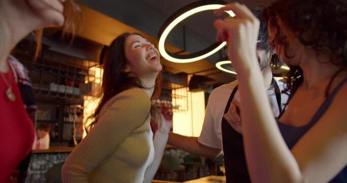 Vibrant Dance Fiesta: Three Joyful Girls Groove with Glasses-Wearing Waiter at a Sunlit Cafe-Bar Bachelorette Party