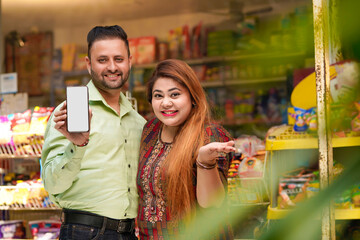 Indian couple showing smartphone screen at grocery shop.