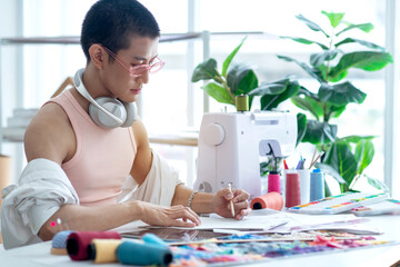 Fashion gay designer with ear phone on neck  working at desk in studio office, Lifestyle Lgbtq...