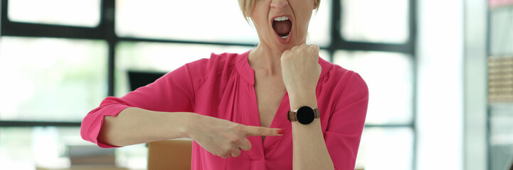 Woman manager screaming and pointing finger at wrist watch in office. Time management and being late at work concept