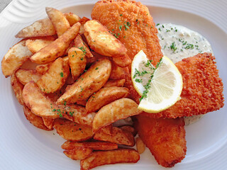 Baked fish with potato wedges on a plate close up high angle view ready to eat