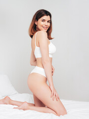 Obraz premium Attractive and relaxed seductive young woman with slim body wearing white underwear. Sexy smiling model lying on sheets in the bedroom at home in the early morning in lingerie. Happy female in bed