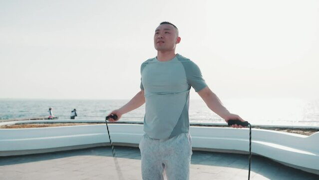 Concentrated asian man jumping rope by sea at dawn