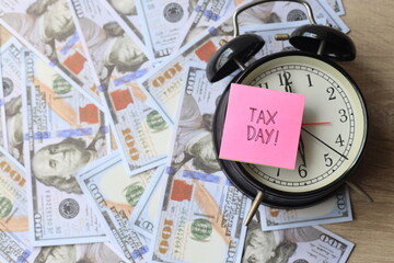 Tax day written on a sticky note against the dollar bills and alarm clock
