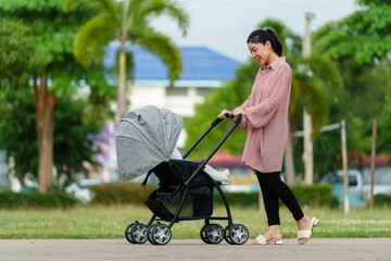 happy mother looking and pushing infant baby stroller while walking in park