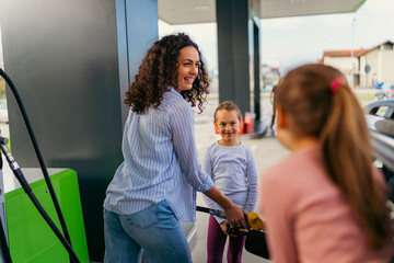 the mother fills the car with fuel at the gas station and talks to her daughters about the upcoming...