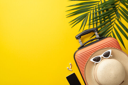 Summer trip concept. Top view photo of orange suitcase with sunhat and sunglasses on it surrounded by palm leaves and phone with headphones on isolated bright yellow background with copy-space - Powered by Adobe