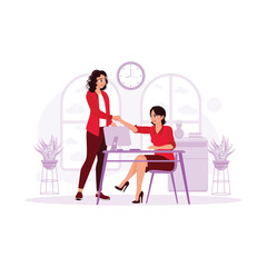 Two women shake hands as a result of the agreement. Two business partners making a deal at a meeting in an office room, in front of a computer, and shaking hands against a window in a calm atmosphere.