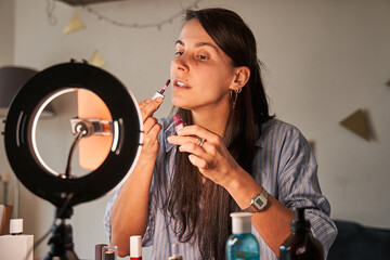 Fototapeta premium Attentive lady with long brunette hair making daily natural makeup and looking at smartphone camera