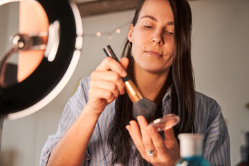 Attentive lady with long brunette hair taking foundation and making daily natural makeup
