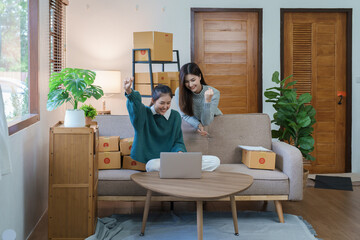 Starting small business entrepreneur of independent Asian woman smiling using computer laptop with cheerful success of online marketing package box items and SME delivery concept