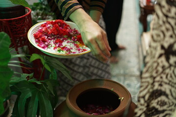 hand holding a many kind of flowers pouring into holy water for showering rituals for preganacy woman