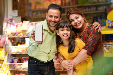 Happy family showing empty smartphone Screen at grocery shop.