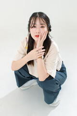 Portrait isolated cutout studio shot of Asian young cute female teenage fashion model with pigtails braids hairstyle in casual trendy wear sitting on floor posing look at camera on white background