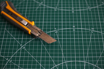 Stationery knife lies on a dark green cutting pad with marking lines for cutting paper and plexiglass.  Cutting board background with a sharp knife