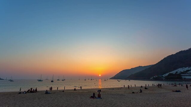 .time lapse golden sky at sunset above the sea at Nai Harn beach..Yachts are on the horizon of the sea during beautiful golden sky..crowd of tourists at Nai Harn beach in wonderful sunset..