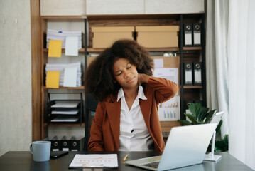 Fototapeta na wymiar Overworked young African businesswoman office worker suffering from neck pain after had a long day at her office desk.