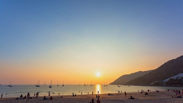 .time lapse golden sky at sunset above the sea at Nai Harn beach..Yachts are on the horizon of the sea during beautiful golden sky..crowd of tourists at Nai Harn beach in wonderful sunset...